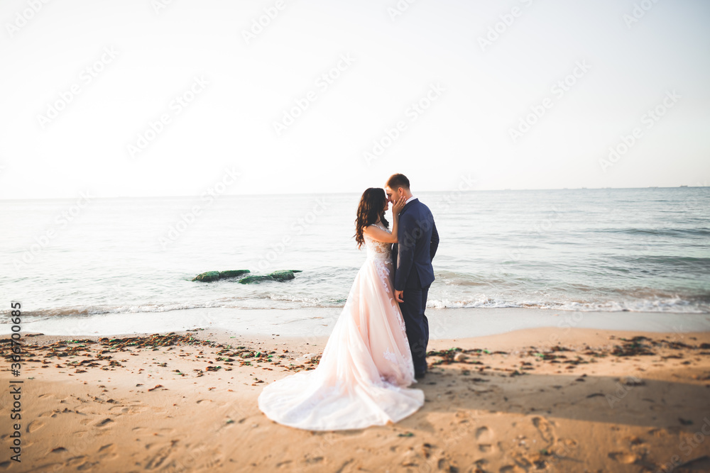 Wedding couple, groom, bride with bouquet posing near sea and blue sky Wedding couple, groom, bride with bouquet posing near sea and blue sky
