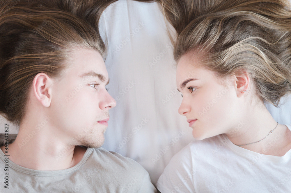 Top view portrait long-haired couple of men and women periling on the bed and looking at each other. The concept of healthy sex and happiness in young families Top view portrait long-haired couple of men and women periling on the bed and looking at each other. The concept of healthy sex and happiness in young families