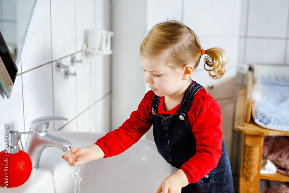 Cute little toddler girl washing hands with soap and water in bathroom. Adorable child learning cleaning body parts. Morning hygiene routine. Happy healthy kid at home or nursery. Cute little toddler girl washing hands with soap and water in bathroom. Adorable child learning cleaning body parts. Morning hygiene routine. Happy healthy kid at home or nursery.