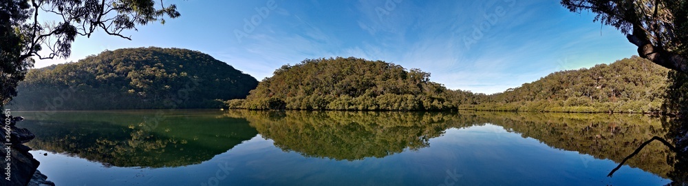 Early morning panoramic view of a calm creek with beautiful reflections of blue sky, mountains and trees on water, Cowan Creek, Bobbin Head, Ku-ring-gai Chase National Park, New South Wales Australia