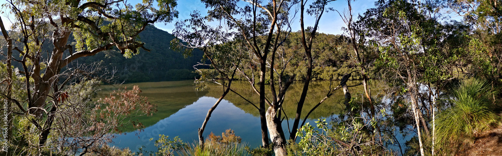 Early morning panoramic view of a calm creek with beautiful reflections of blue sky, mountains and trees on water, Cowan Creek, Bobbin Head, Ku-ring-gai Chase National Park, New South Wales Australia