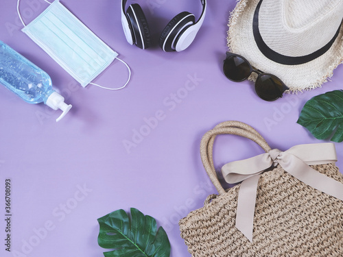 COVID-19 prevention , travel and new normal concept, top view of woven bag with surgical mask and alcohol gel and women's vacation accessories on purple background.