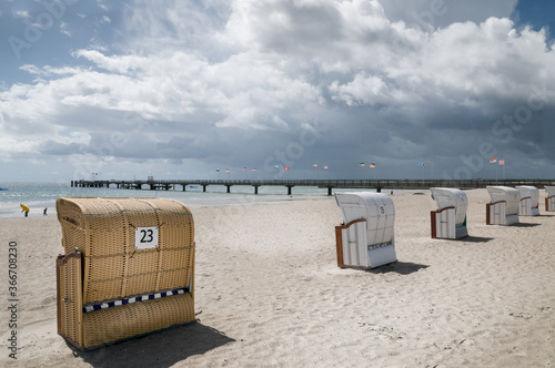 Empty beach chairs on the Baltic Sea beach and pier with the flags of German constituent states and cities. Grossenbrode, Schleswig- Holstein, Germany