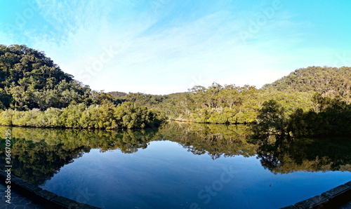 Early morning panoramic view of a calm creek with beautiful reflections of blue sky, mountains and trees on water, Cockle Creek, Bobbin Head, Ku-ring-gai Chase National Park, New South Wales Australia © Ivan