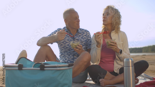 Senior happy couple on picnic eating salad relaxing on sea beach