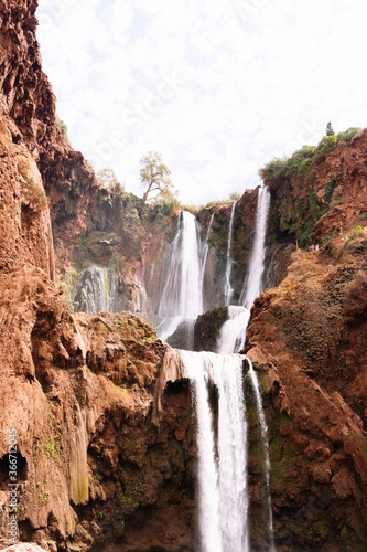 Vertical photo of water falling from Ouzoud waterfalls in an arid terrain.
