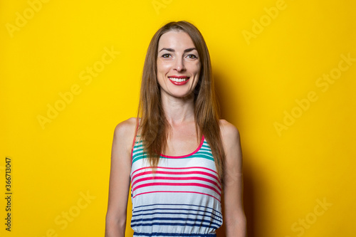 Friendly smiling young woman in a striped dress on a yellow background.