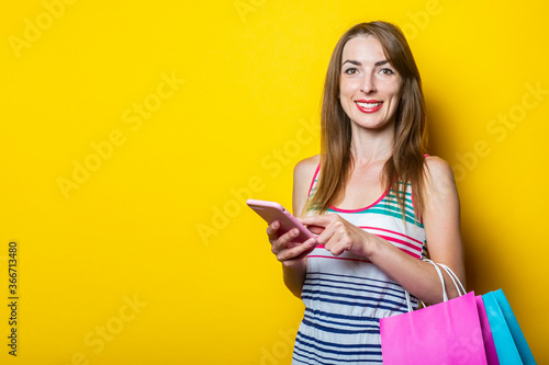 Beautiful young woman with phone and shopping bags on yellow background.