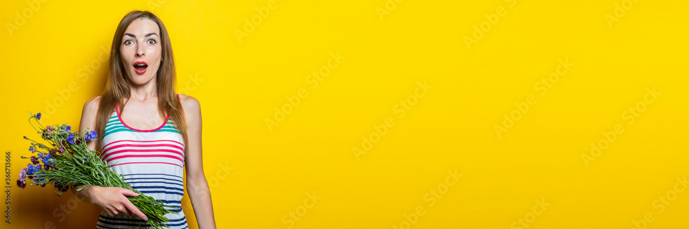 Surprised young woman in striped dress holding wildflowers on yellow background. Banner. Surprised young woman in striped dress holding wildflowers on yellow background. Banner.