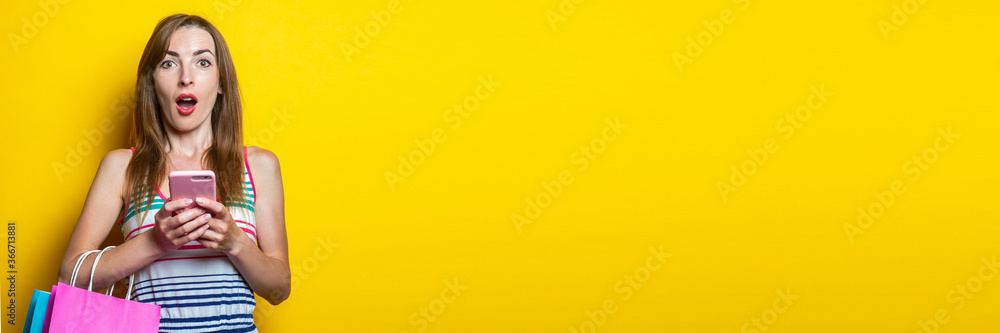 Surprised shocked young woman with phone and shopping bags on yellow background. Banner. Surprised shocked young woman with phone and shopping bags on yellow background. Banner.