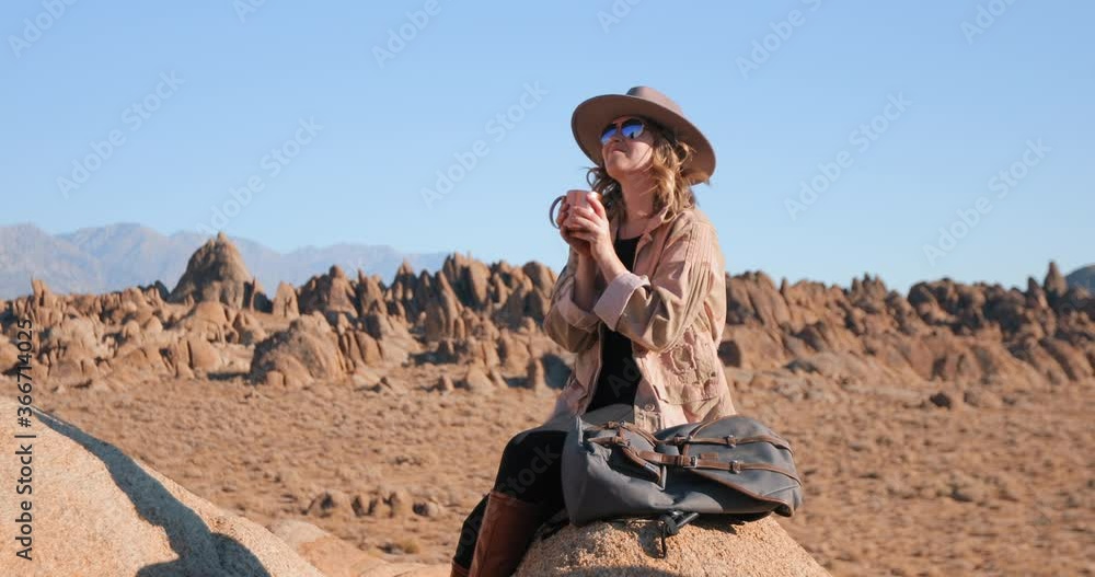 A happy beautiful woman is drinking water and enjoying peaceful sunrise in wilderness nature. Girl in hat and sunglasses, wind is blowing her blonde hair. Scenic rocky landscapes on motion background A happy beautiful woman is drinking water and enjoying peaceful sunrise in wilderness nature. Girl in hat and sunglasses, wind is blowing her blonde hair. Scenic rocky landscapes on motion background