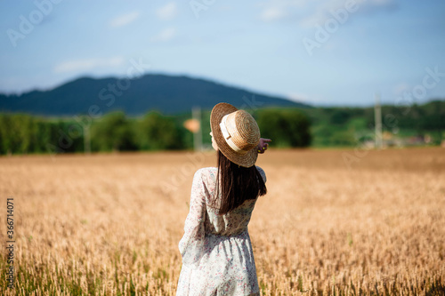 Portrait of a girl from the back in a wheat field. Portrait of a beautiful girl in a white dress and hat on a wheat field. Girl in a white dress and hat. Wheat field.