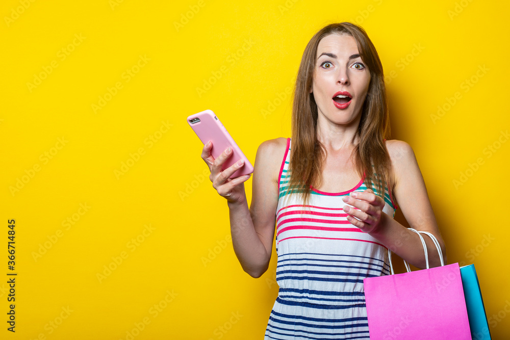 Surprised shocked young girl with phone and shopping bags on yellow background. Surprised shocked young girl with phone and shopping bags on yellow background.