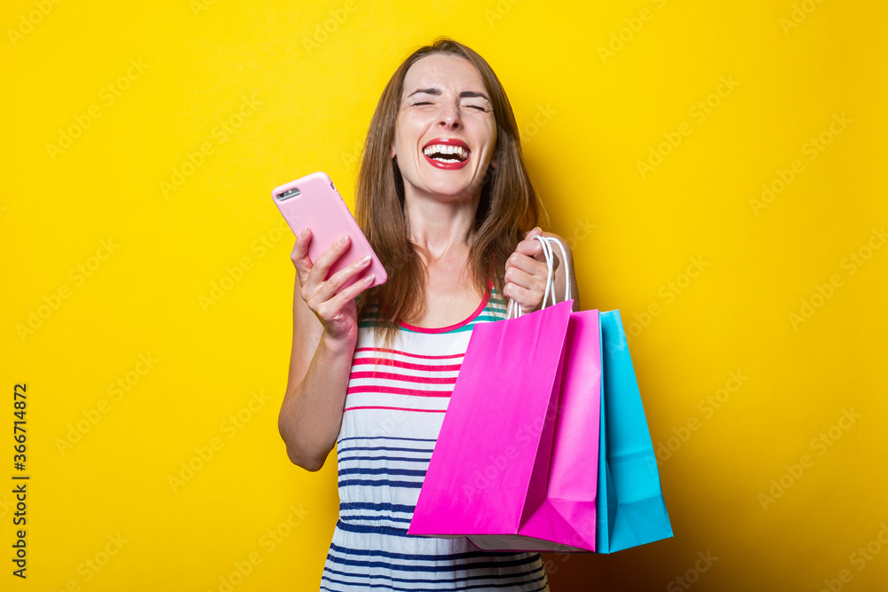 Joyful young girl with phone holding shopping bags on yellow background. Joyful young girl with phone holding shopping bags on yellow background.