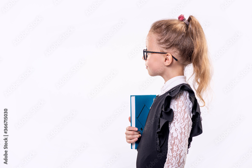 Little schoolgirl in glasses stands on a white background and holds a book, copy free space. Little schoolgirl in glasses stands on a white background and holds a book, copy free space.