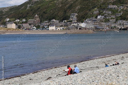 People sitting on a shingle beach  enjoying the view of Barmouth  across the mouth of the Mawddach river in Gwynedd, Wales, UK. photo