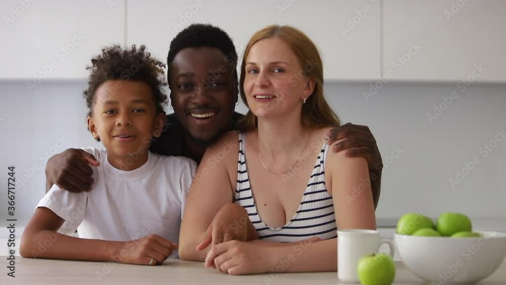 portrait of happy interracial family of three. Spbi couple and mixed race son sit at kitchen and look at camera. teenager son with parents. black dad hugging caucasian mom portrait of happy interracial family of three. Spbi couple and mixed race son sit at kitchen and look at camera. teenager son with parents. black dad hugging caucasian mom