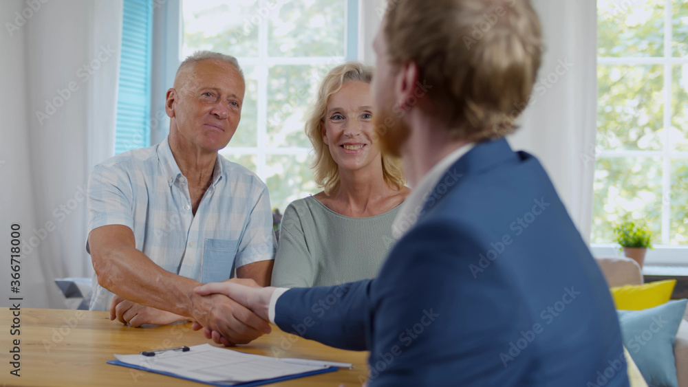 Obraz premium Real estate agent giving handshake to smiling elderly couple after successful agreement