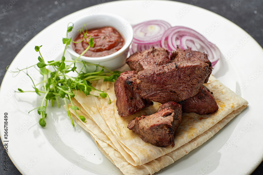 Fried shish kebab with lavash, sauce, microgreen and onion, on a white plate, on a gray background Fried shish kebab with lavash, sauce, microgreen and onion, on a white plate, on a gray background