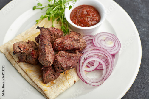 Fried shish kebab with lavash, sauce, microgreen and onion, on a white plate, on a gray background