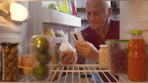 Schilderij op canvas Senior man taking yogurt from fridge for snack checking expiry data