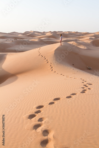 Blonde female Caucasian traveler leaving footprints in sand dunes when walking in dessert in Oman.