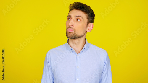 Handsome bearded man looks away on yellow background with copy space. Guy in light blue shirt looks in place for text or goods