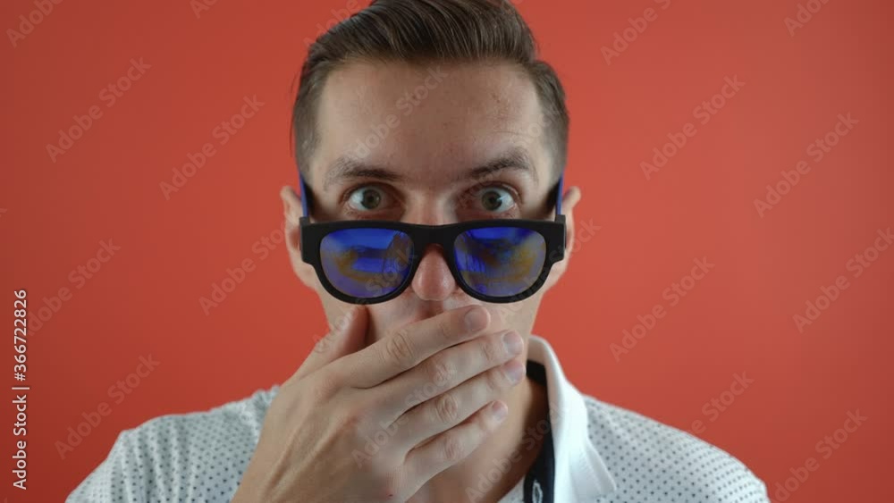 Stylish young man shocked and surprised on red color background. Man hipster in surprise shoots sunglasses and looks at the camera in surprise. Stylish young man shocked and surprised on red color background. Man hipster in surprise shoots sunglasses and looks at the camera in surprise.