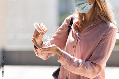 Woman cleaning her hands with sanitizer in the street.