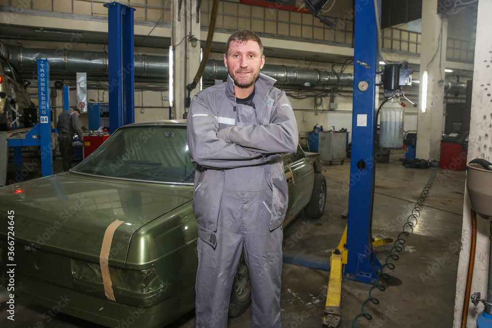 a male mechanic stands against the background of a garage