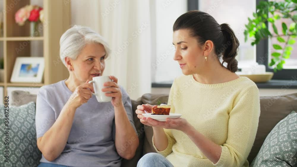 family, generation and people concept - happy smiling senior mother and adult daughter eating cake with coffee at home family, generation and people concept - happy smiling senior mother and adult daughter eating cake with coffee at home