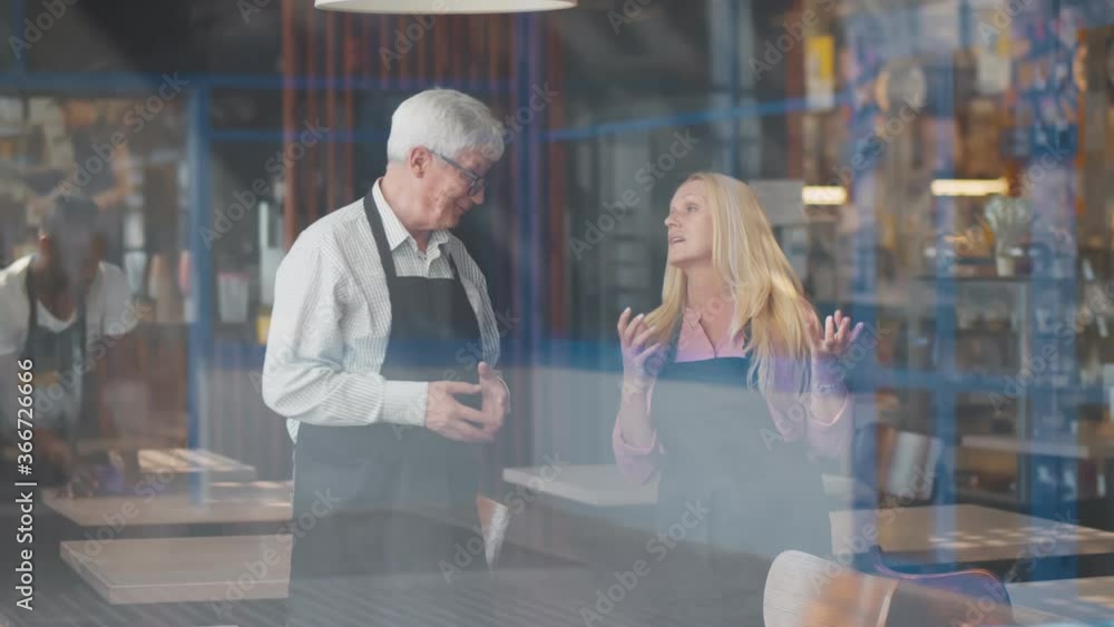 View through window of mature couple cafe owners discussing business development View through window of mature couple cafe owners discussing business development