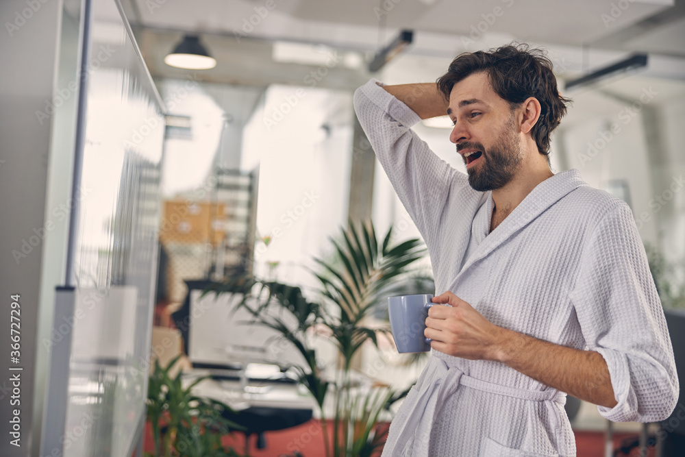 Fototapeta premium Sleepy young man yawning and holding cup of coffee