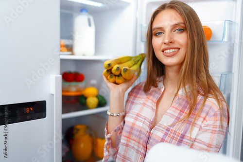 Portrait of a young blonde woman taking food from her fridge