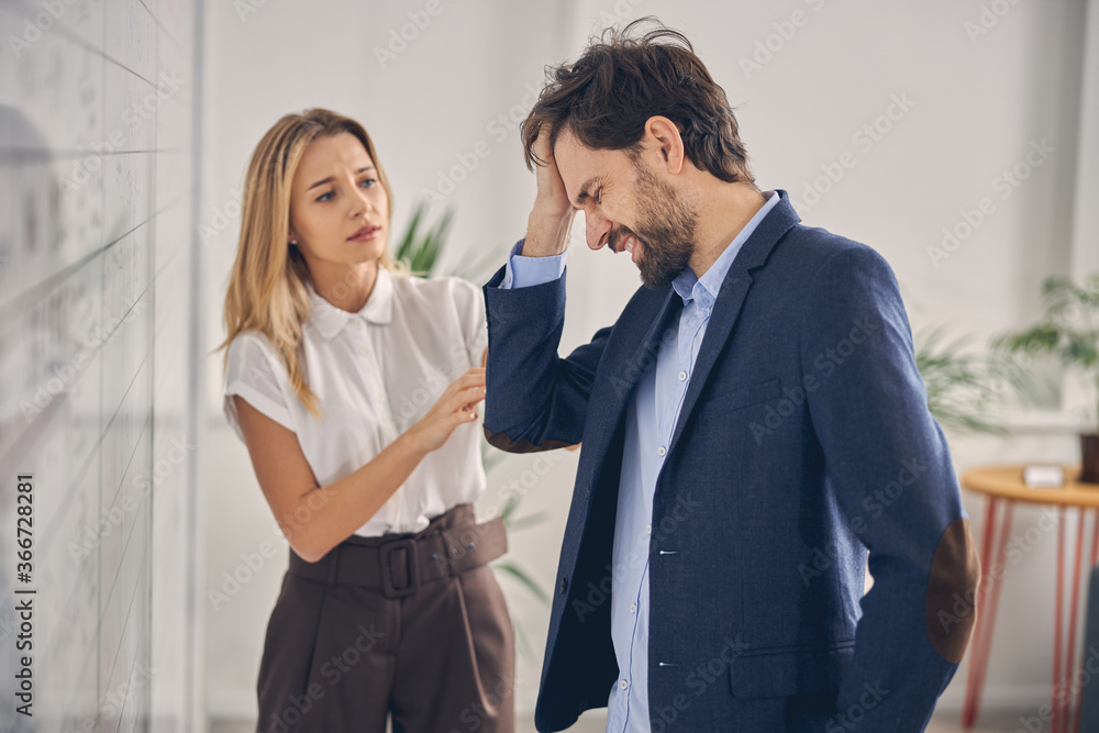 Bearded man having headache while working with lady in office Bearded man having headache while working with lady in office