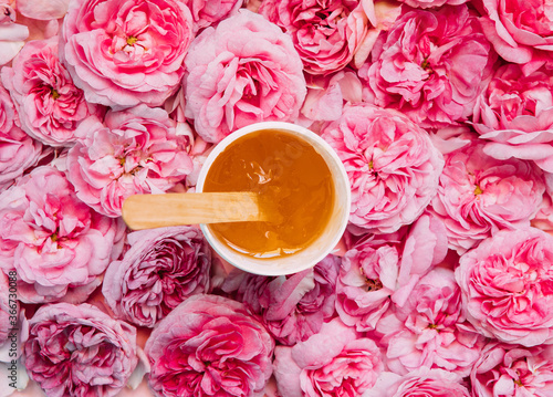 depilation and beauty concept - sugar paste or wax honey for hair removing flows down from wooden waxing spatula sticks on flower background. copyspase