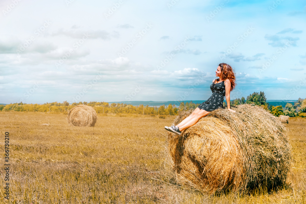 Country concept young woman sitting on haystack in summer Country concept young woman sitting on haystack in summer
