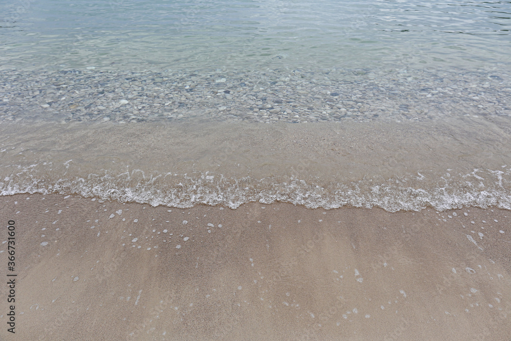 Top view shot of soft wave licking sandy beach shore on cloudy day. Ocean scenery with calm translucent water and clean sand, a lot of copy space for text. Close up. Top view shot of soft wave licking sandy beach shore on cloudy day. Ocean scenery with calm translucent water and clean sand, a lot of copy space for text. Close up.