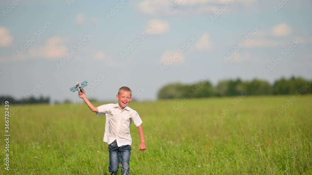 Happy Smiling boy child with Wooden Toy Plane Model Runs in Summer Field on Blue Sky Background. Childhood dreams. Concept travel and freedom. SLOW MOTION Happy Smiling boy child with Wooden Toy Plane Model Runs in Summer Field on Blue Sky Background. Childhood dreams. Concept travel and freedom. SLOW MOTION