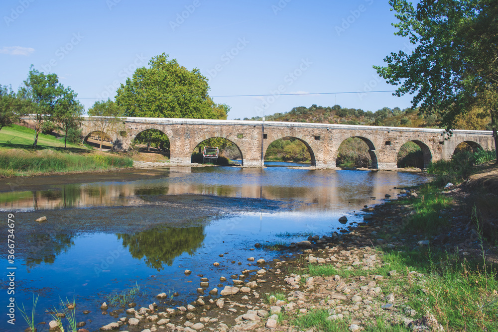 Pillars of an old stone bridge over a dried riverbed in the summer. Empty river bed with poisoned muddy water with low water level. Prolonged drought. 