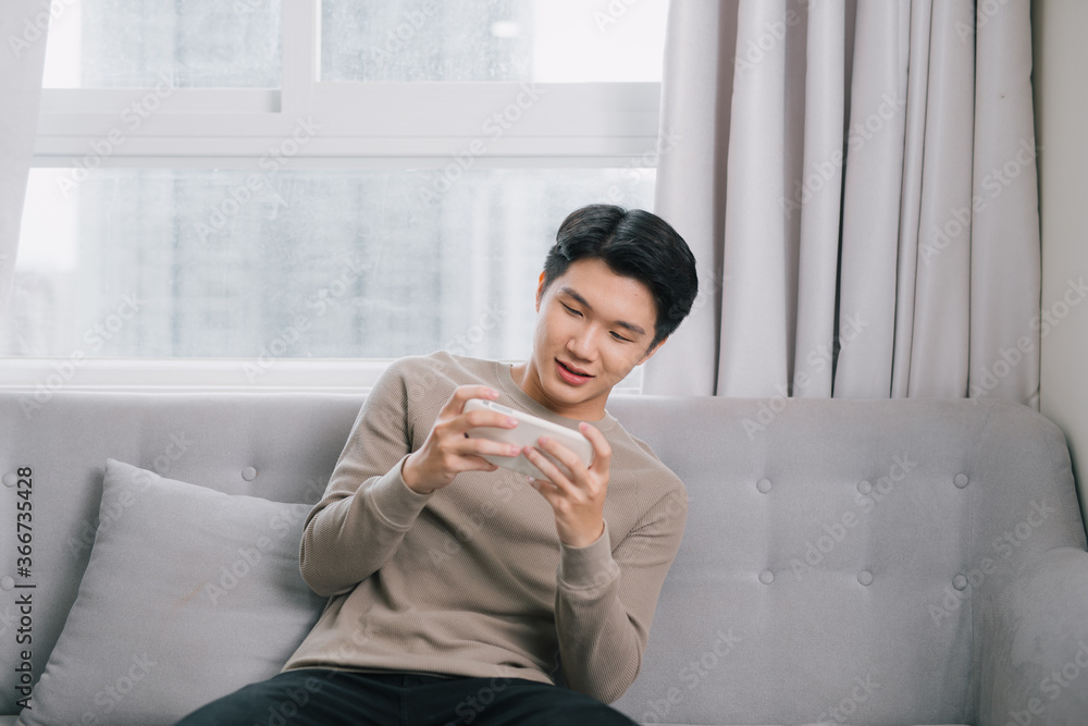 Asian young man is seriously playing the game on his smartphone on the couch. Asian young man is seriously playing the game on his smartphone on the couch.