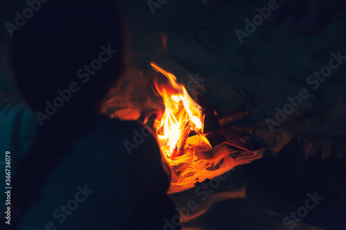 Fireplace on the beach at night. Little girl sitting near the fire with wood, flames in the nature at night.