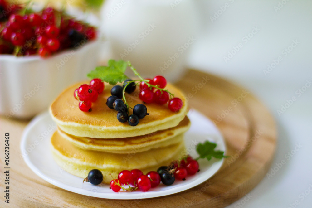 Summer breakfast pancakes with red and black currants in a bowl and milk in a glass jug on a white background Summer breakfast pancakes with red and black currants in a bowl and milk in a glass jug on a white background