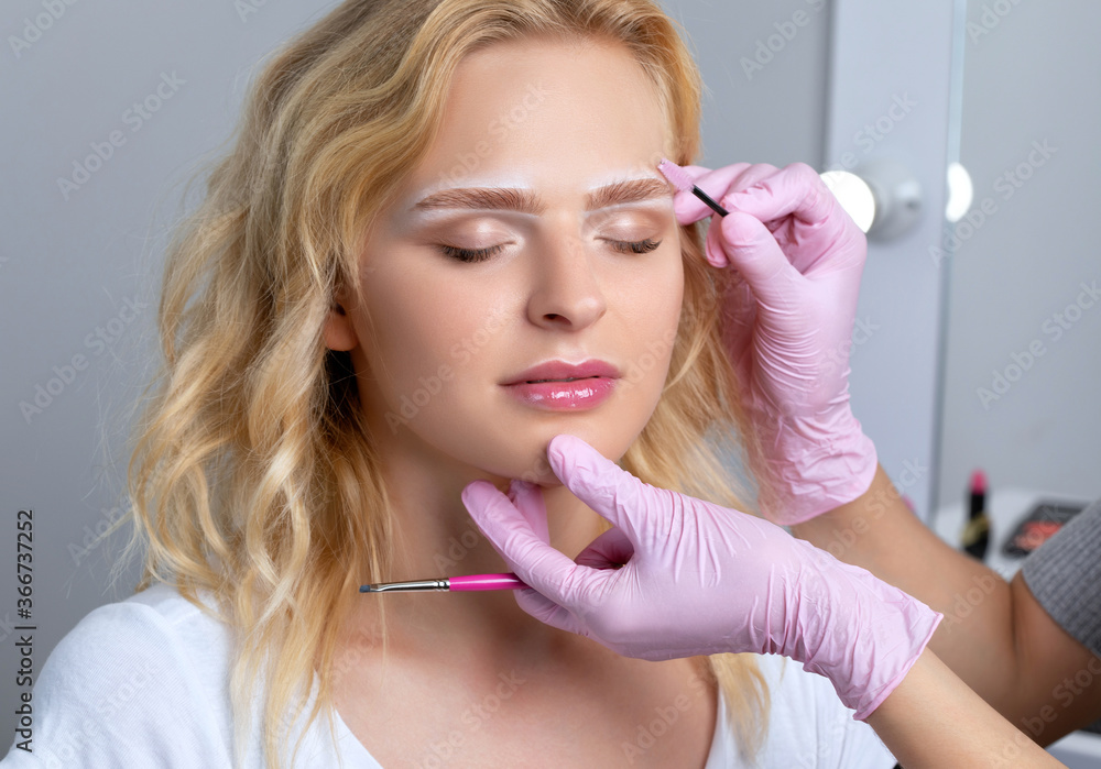 Blonde woman having permanent make-up tattoo on her eyebrows. Closeup beautician doing tattooing eyebrow.Professional makeup and cosmetology skin care.