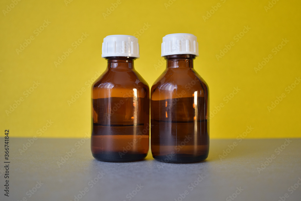 Two brown cosmetic bottles with a white lid on a gray-yellow background Two brown cosmetic bottles with a white lid on a gray-yellow background