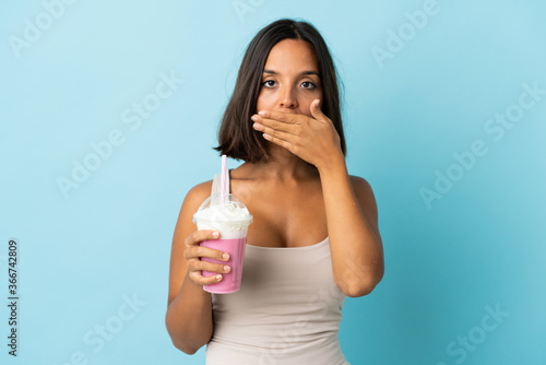 Young woman with strawberry milkshake isolated on blue background covering mouth with hand
