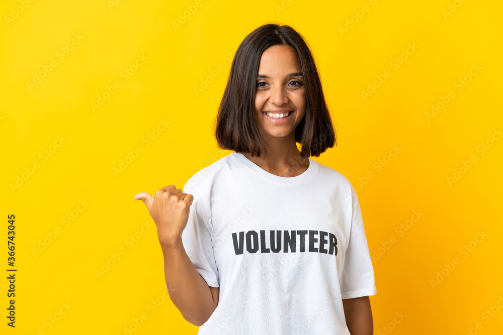 Young volunteer woman isolated on yellow background pointing to the side to present a product Young volunteer woman isolated on yellow background pointing to the side to present a product