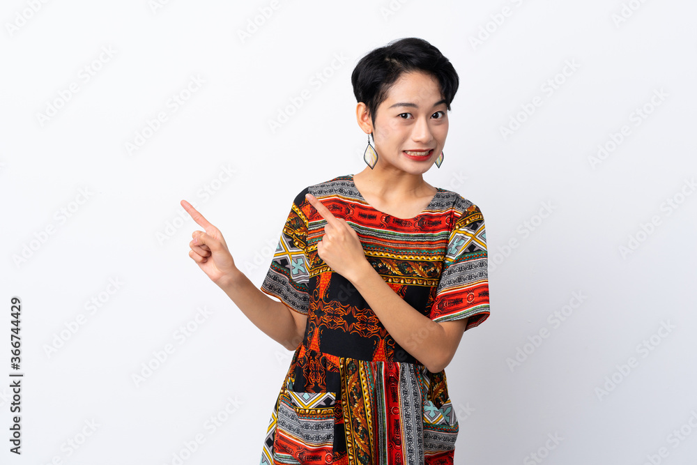 Young Asian girl with a colorful dress over isolated white background frightened and pointing to the side Young Asian girl with a colorful dress over isolated white background frightened and pointing to the side