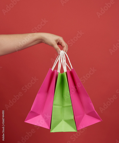 woman holds stack of paper bags on red background, shopping concept