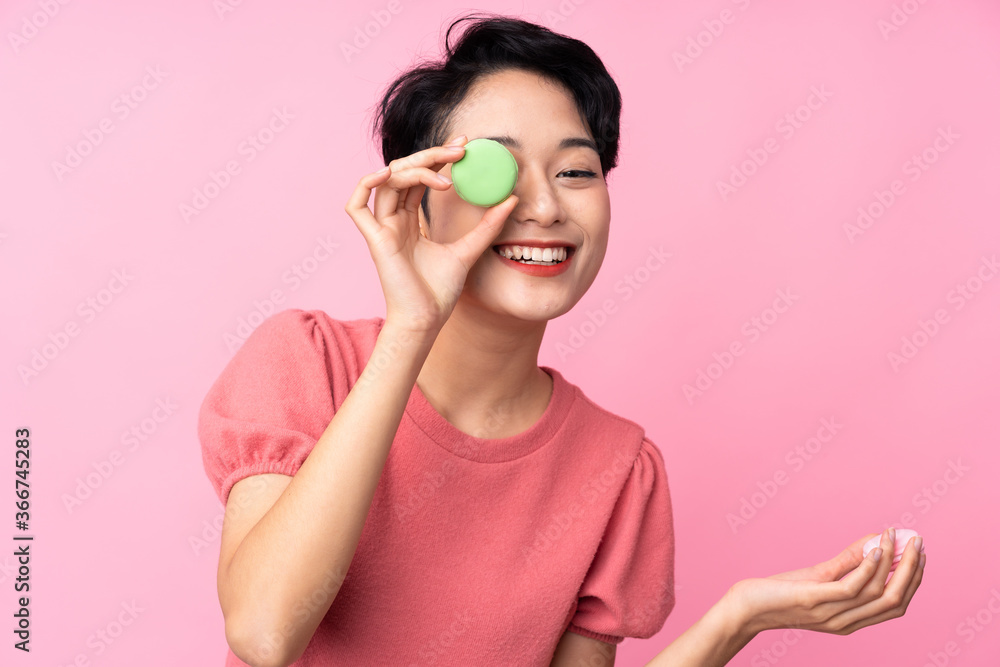 Young Asian girl over isolated pink background holding colorful French macarons Young Asian girl over isolated pink background holding colorful French macarons